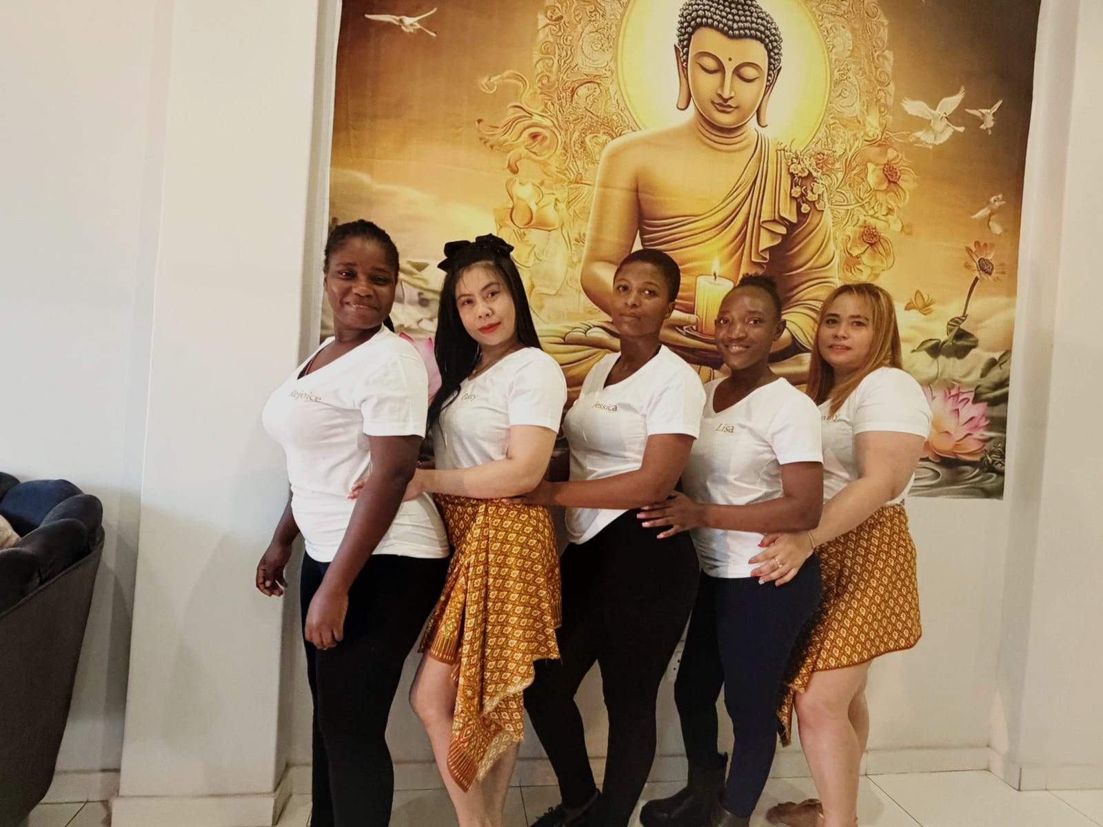 Natnaree Thai Spa team posing together in front of a golden Buddha tapestry in the treatment lounge